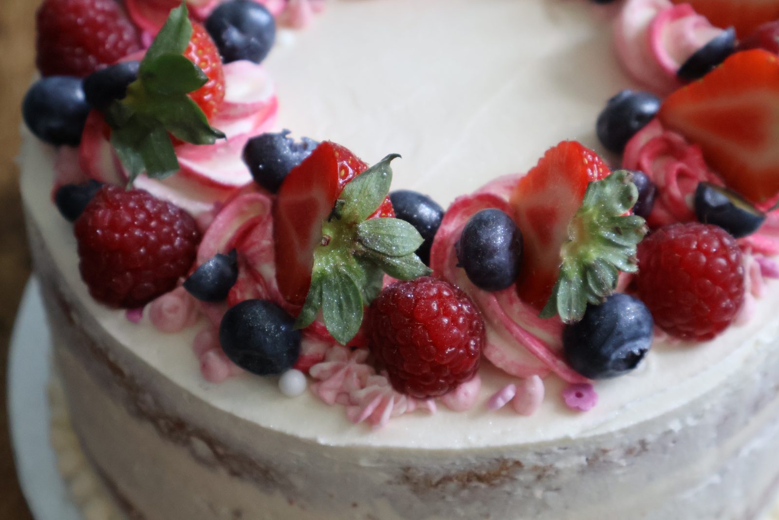Close-up of fresh strawberries, raspberries and blueberries on pink buttercream swirls