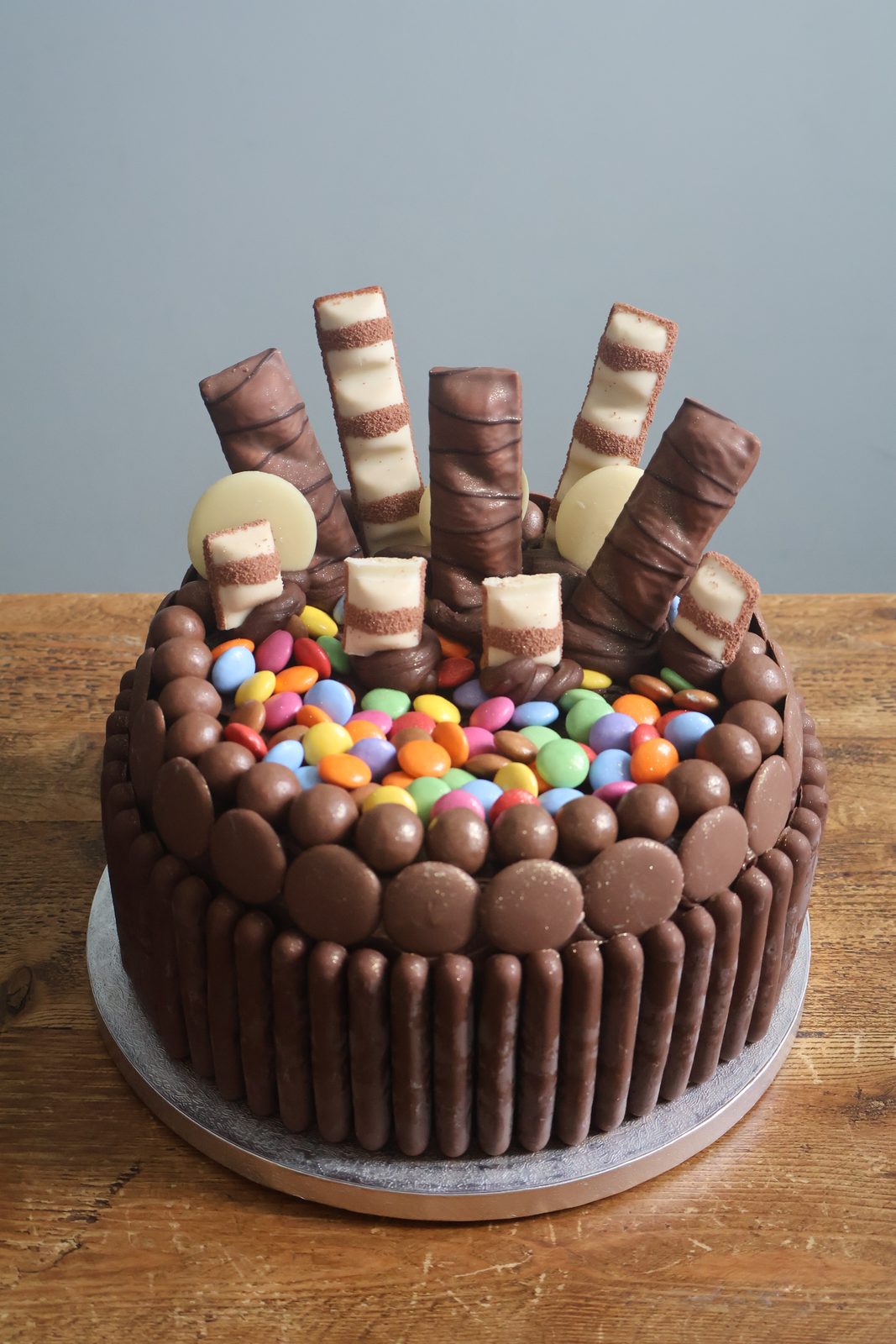 Chocolate cake ringed with chocolate fingers and buttons, filled with Smarties and topped with Kinder bars