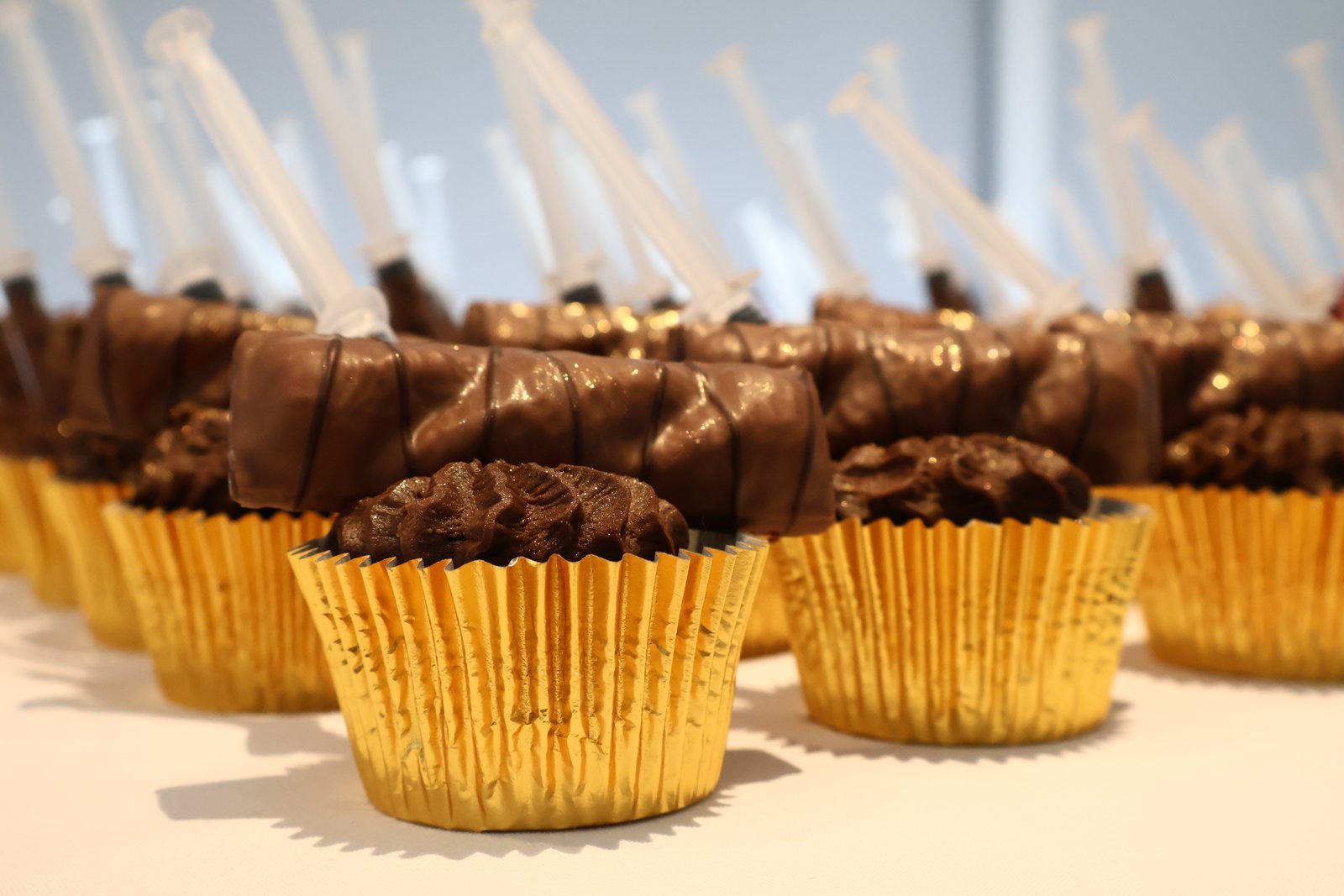 Close-up of a chocolate cupcake in a gold case with a chocolate bar and a syringe on top