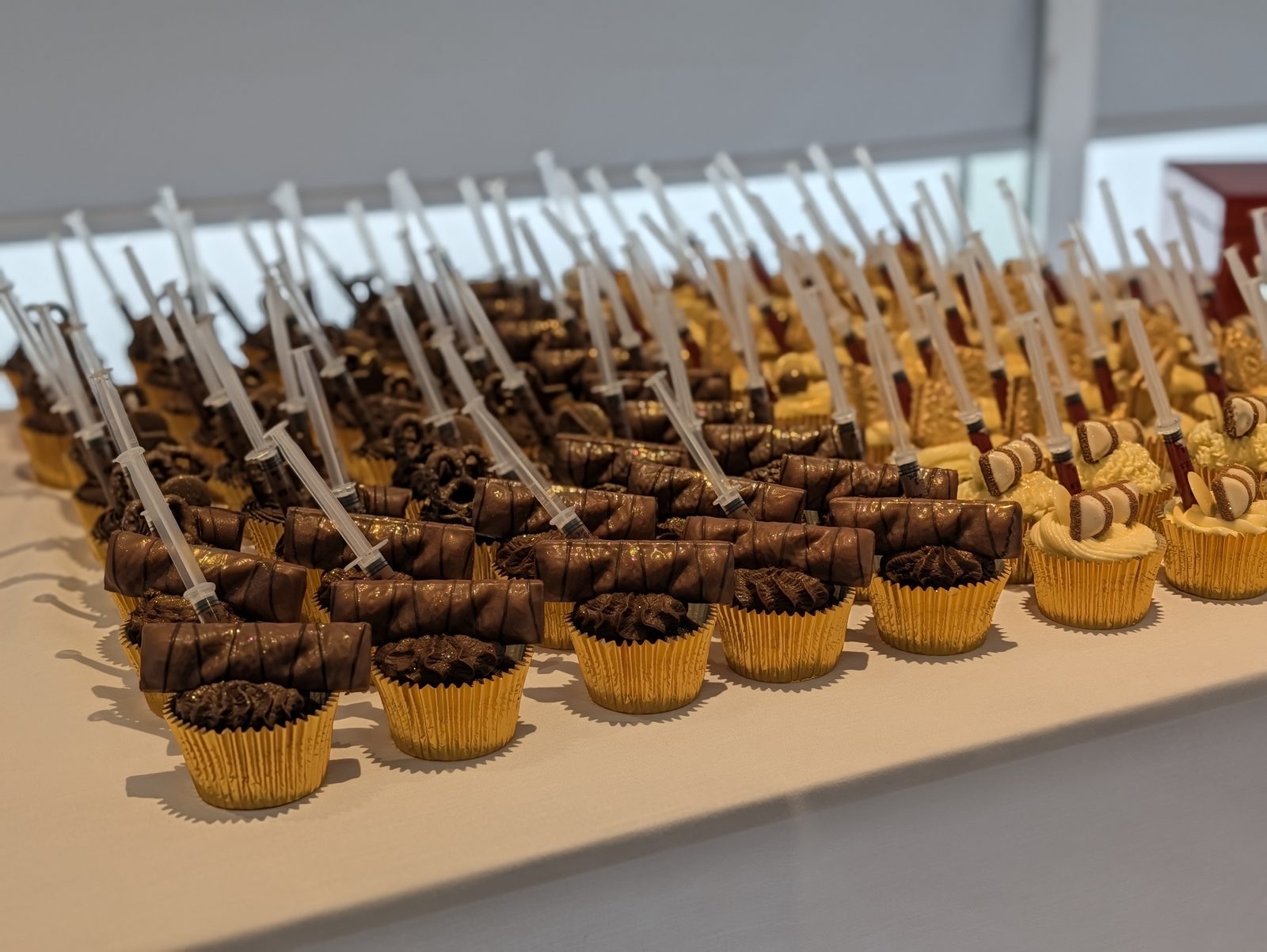 Display of novelty cupcakes with chocolate and vanilla buttercream, chocolate bars and syringes